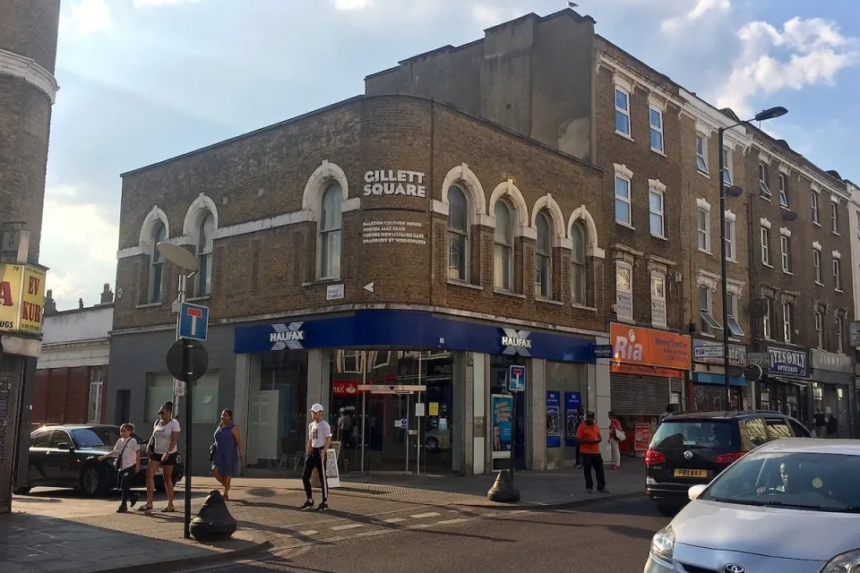 Intersection with sign for Gillett Square in East London, UK with brick buildings with ground floor storefronts.